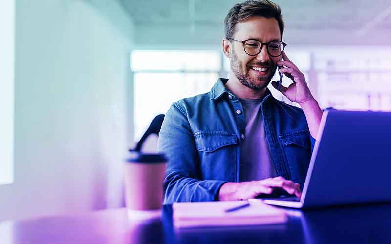 Junger Mann telefoniert und arbeitet am Laptop in moderner Büroumgebung – Recruiting bei Printus