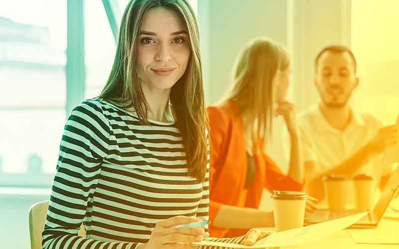 Junge Frau mit gestreiftem Oberteil sitzt mit anderen Schüler:innen an einem Tisch – Gruppenarbeit bei Printus