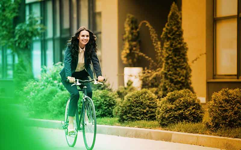 Junge Frau in Businesskleidung fährt lachend Fahrrad – Sinnbild für umweltfreundliche Mobilität und moderne Arbeitskultur bei Printus
