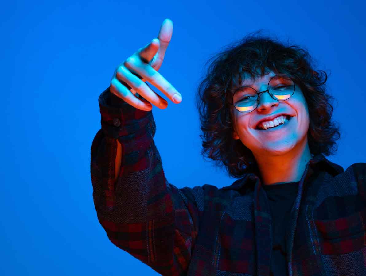 Lachender Jugendlicher mit Brille und lockigem Haar zeigt locker in die Kamera – Motiv für Printus-Recruitingübersicht für Schüler:innen