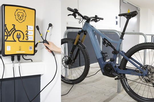 E-Bike an einer gelben Ladestation mit mehreren Ladeanschlüssen bei Printus – umweltfreundliches Mobilitätsangebot für Mitarbeitende